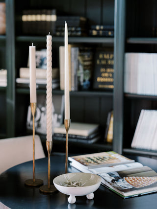 Handcrafted Antique Brass Candlesticks by CG Hunter, beautifully arranged with textured ivory candles on a chic black table surrounded by curated books.