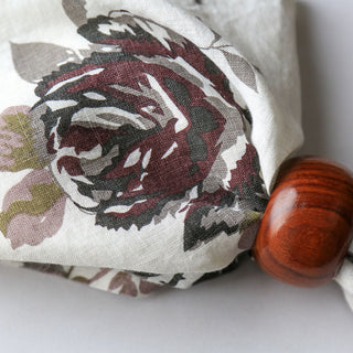 Close-up of CG Hunter Handcrafted Linen Eggplant and Grey Roses Napkins featuring intricate grey rose designs against a rich eggplant background with a polished wooden ring, embodying luxury and elegance.