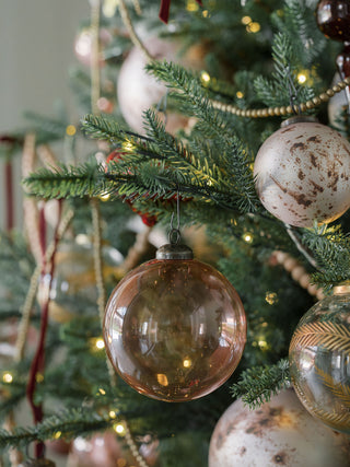 A stunning shiny vintage rose glass ornament nestled among a decorated Christmas tree, showcasing its charming blush tone, created by CG Hunter.