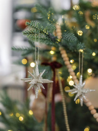 Two exquisite 2.75" Gold Glitter Starburst Ornaments by CG Hunter, gracefully adorning a beautifully decorated Christmas tree with warm lights.