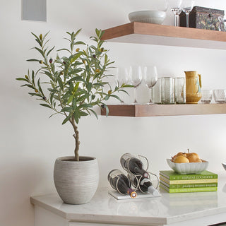 Elegant lifestyle image featuring the artificial Olive Topiary Tree with Mediterranean Pot by CG Hunter, artistically placed on a minimalist kitchen countertop surrounded by glassware and decor.