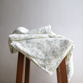 Elegant CG Hunter Grey and Green Lilies Linen Tablecloth artistically arranged on a stool, revealing the delicate floral patterns that add charm to dining decor.