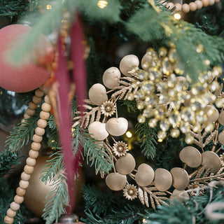 A close-up of a luxurious 7.5" Iron Wreath Ornament in brass finish by CG Hunter, elegantly displayed among festive holiday decorations, featuring rich greenery and vibrant ornaments.