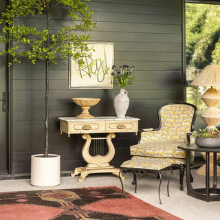 CG Hunter 8' faux olive tree styled in a white planter beside a vintage lyre console table and patterned armchair against a dark green shiplap wall