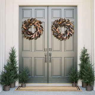 CG Hunter faux brown magnolia leaf wreaths on double front doors with faux pine trees in baskets, farmhouse Christmas decor