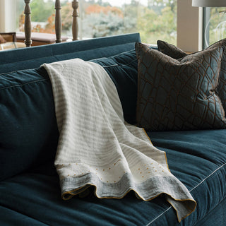 Luxurious ivory throw blanket draped elegantly over a dark blue sofa, embodying the essence of CG Hunter's Gifts for the Homebody collection. Ideal for homebody gift ideas, this soft linen throw adds warmth and style to any relaxed living space.