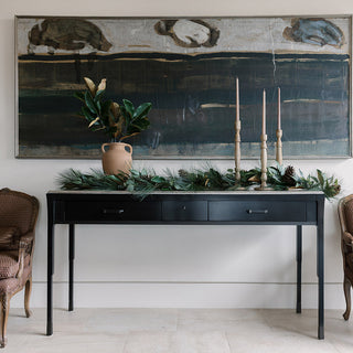 Elegant home decor setting featuring a stylish black console table adorned with a lush greenery centerpiece, candles, and a decorative vase. Perfect inspiration for gifts for the decor enthusiast, showcasing sophisticated decor enthusiast gifts.