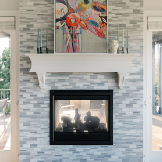 Stylish mantel showcasing CG Hunter's 3.5" Iron Candleholders in Antique Brass with taper candles, framed by vibrant artwork and a sleek fireplace on a textured grey wall.