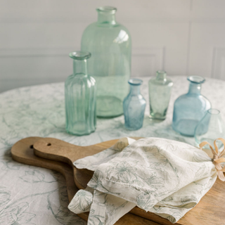 Elegant setting featuring CG Hunter's Assorted Blue and Green Glass Bud Vases artfully arranged on a table with a floral-themed linen, showcasing unique shapes and calming hues.