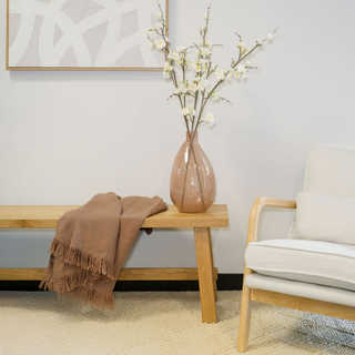 Chic living room adorned with the CG Hunter Handmade Hammered Glass Vase in Peach, holding delicate branches, highlighting its timeless design and elegance on a stylish wooden bench.