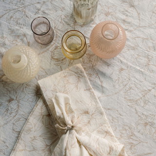 Chic arrangement of delicate glassware over a CG Hunter Blush Lilies Tablecloth, showcasing the sophisticated design of matching napkins for an elevated dining experience.