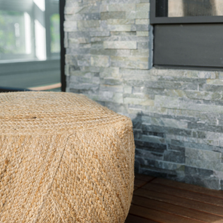 Square Braided Jute Ottoman Pouf by CG Hunter against a stone backdrop, emphasizing its sophisticated texture and versatility in home decor.
