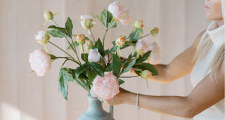 Person holding a bouquet of pink flowers in a vase against a neutral background