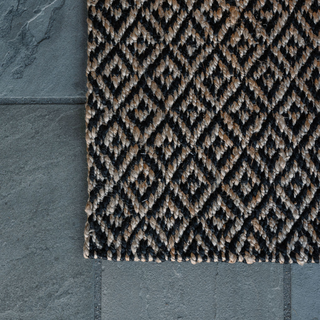 Corner close-up of CG Hunter Natural and Black Diamonds Jute Rug on a stone surface, showcasing its elegant design and texture.