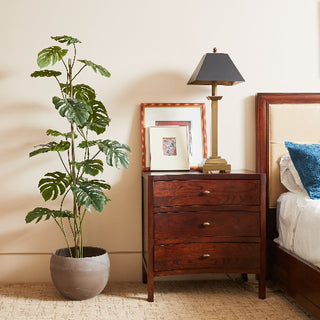 Sophisticated 5' Artificial Monstera Tree by CG Hunter positioned gracefully next to a sleek nightstand and ambient lamp, highlighting contemporary home decor.