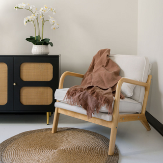 CG Hunter Natural and Brown Round Braided Jute Rug complementing an armchair draped with a warm blanket. This handcrafted rug adds natural elegance and texture to any luxurious living space.