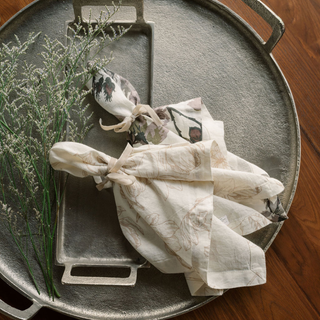 Elegant setting featuring CG Hunter Handcrafted Linen Eggplant and Grey Roses Napkins, with floral napkin presentation on a textured tray, enhancing dining sophistication.