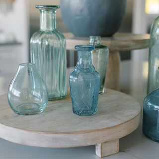 Stylish close-up of CG Hunter blue and green glass bud vases positioned on a wooden display, showcasing their artisanal quality and timeless beauty.
