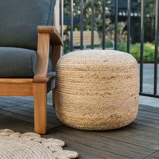 CG Hunter Round Braided Jute Ottoman Pouf elegantly placed beside a modern wooden chair on a stylish patio, showcasing its natural texture and artisanal design.