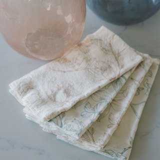 Set of four CG Hunter Blush Lilies Napkins arranged stylishly, showcasing linen fabric with delicate floral patterns.