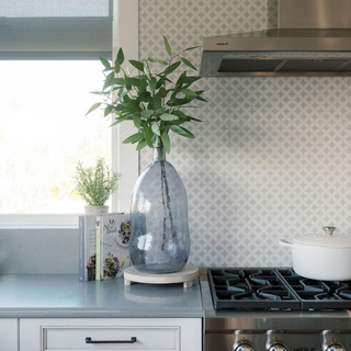 Elegant CG Hunter Hammered Glass Vase in Smoke displayed in a modern kitchen setting, showcasing its smoky gray hue and unique hammered texture, surrounded by greenery.