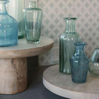 Sophisticated collection of CG Hunter handcrafted blue and green glass bud vases on sleek wooden pedestals, adding a touch of elegance to modern decor.