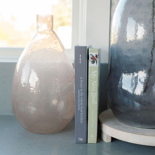 A close-up view of the CG Hunter Handmade Hammered Glass Vase in Peach beside two decorative books, emphasizing its exquisite texture and soft glow, perfect for luxury home decor.