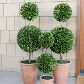 Five potted artificial topiary plants against a tiled wall.