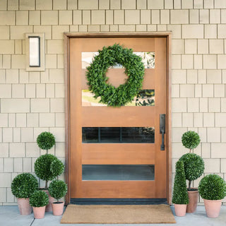 Wooden front door with a wreath, surrounded by potted plants on a tiled wall background