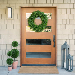 Wooden front door with a wreath, potted plants, and a lantern on a tiled wall background