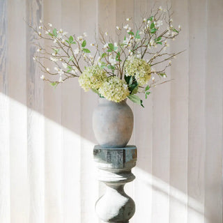 Decorative vase with branches and flowers on a pedestal against a striped wall.