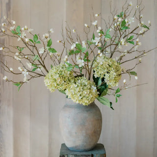 Decorative floral arrangement with green and white flowers in a textured vase on a neutral background