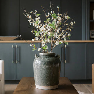 Decorative vase with white flowers on a wooden table against a dark wall.