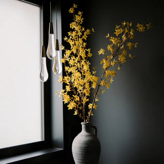 Gray vase with yellow flowers next to a window with black frame
