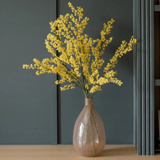 Vase with yellow flowers on a wooden surface against a dark gray wall