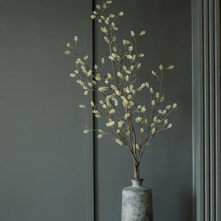 Artificial plant in a textured vase against a dark gray wall