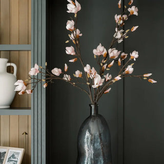 Decorative vase with pink floral branches against a dark wall