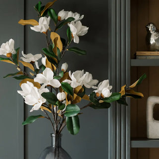 Artificial flower arrangement with white flowers and green leaves in a clear vase against a dark background.