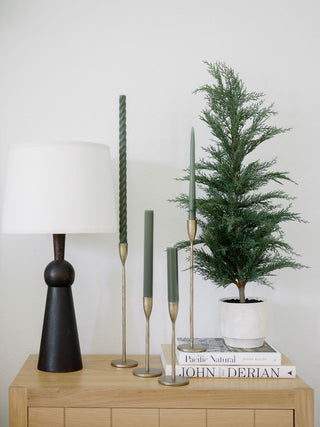 Handcrafted Antique Brass Candlesticks by CG Hunter, elegantly displayed beside a decorative lamp and a lush green plant on a stylish wooden surface.