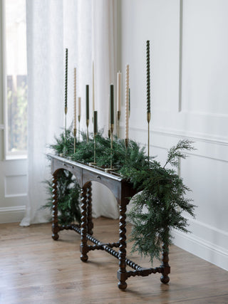 Elegant display of handcrafted antique brass candlesticks by CG Hunter, showcasing a sophisticated arrangement of various candle heights amidst beautiful greenery.
