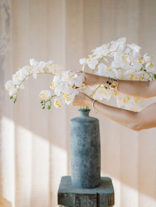 Person holding white orchids next to a gray vase against a neutral background