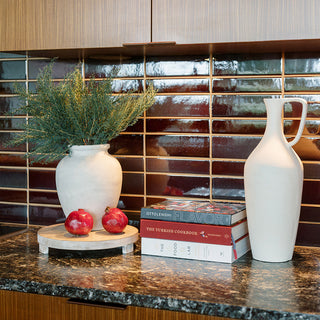 Luxurious display featuring the Charlotte Wood Cheese Board by CG Hunter, elegantly positioned with a vase, greenery, and decorative books on a polished countertop, enhancing the aesthetic of modern entertaining.
