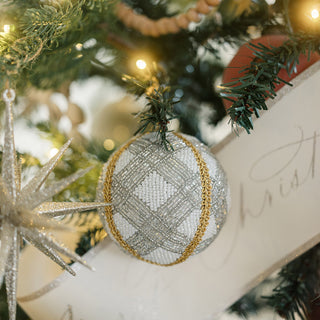 A stunning detail of a shimmery round jute Christmas ornament by CG Hunter, adorned with a chic pattern and set amidst lush greenery, embodying a blend of contemporary style and festive spirit.