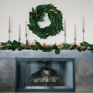 Chic 30" Faux Green Magnolia Leaf Wreath by CG Hunter beautifully showcased above a modern fireplace, complemented by sleek candlesticks and decorative elements.