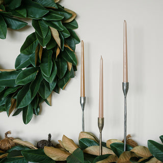Close-up of the 9' Faux Green Magnolia Leaf Garland by CG Hunter, beautifully displayed alongside tall, taper candles on a minimalistic wall background.