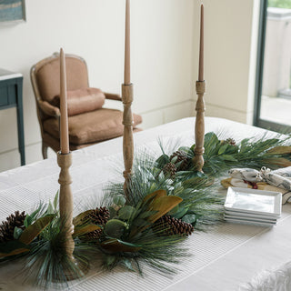 Chic dining centerpiece adorned with the Magnolia, Eucalyptus, Pinecone, & Needle Pine Garland by CG Hunter, surrounded by elegant candlesticks.