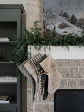 Elegant mantel adorned with stockings and CG Hunter cedar garland, creating a warm and inviting holiday atmosphere.