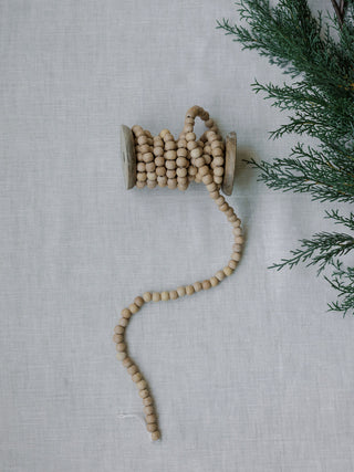 Natural Wood Handmade Bead Garland on Spool by CG Hunter, displayed on a soft linen backdrop, showcasing its artisanal craftsmanship.