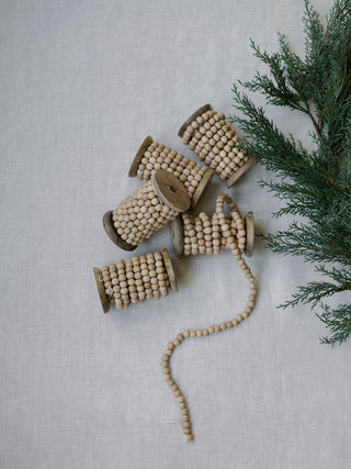 Natural Wood Handmade Bead Garland on Spool by CG Hunter, featuring multiple spools artfully arranged with greenery, ideal for festive styling.
