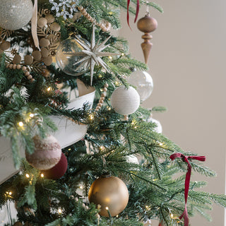 An elegant close-up of a beautifully decorated Christmas tree featuring shimmery round jute ornaments by CG Hunter, harmonizing festive charm with artisanal quality for a sophisticated holiday look.